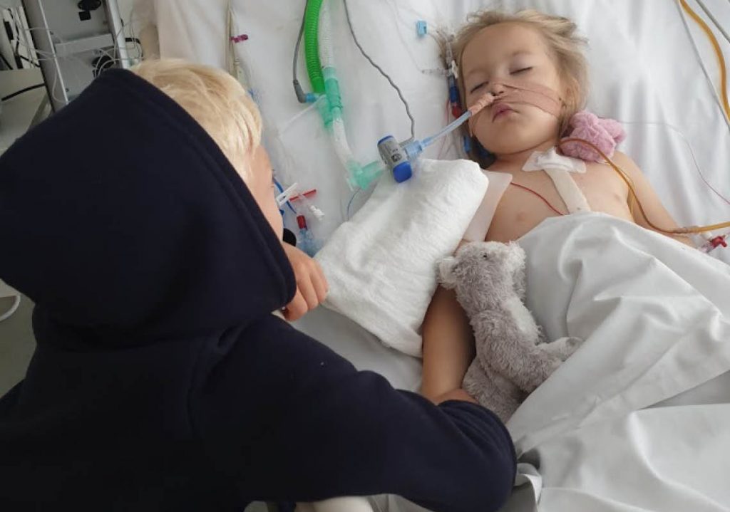 Ellie håller sin bror i handen i sjukhussängen