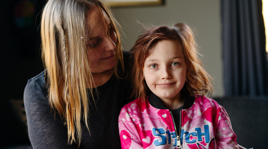Nelly har en rosa tröja och sitter bredvid sin mamma
